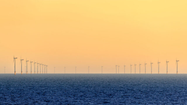 Line of wind turbines on the sea horizon against an orange sunset