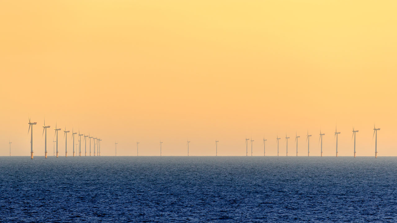 Line of wind turbines on the sea horizon against an orange sunset