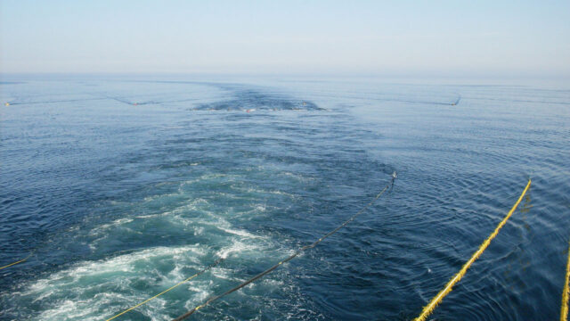 A view across the sea with yellow tow ropes connected to equipment below the surface which is creating a trail in the water as it is towed along