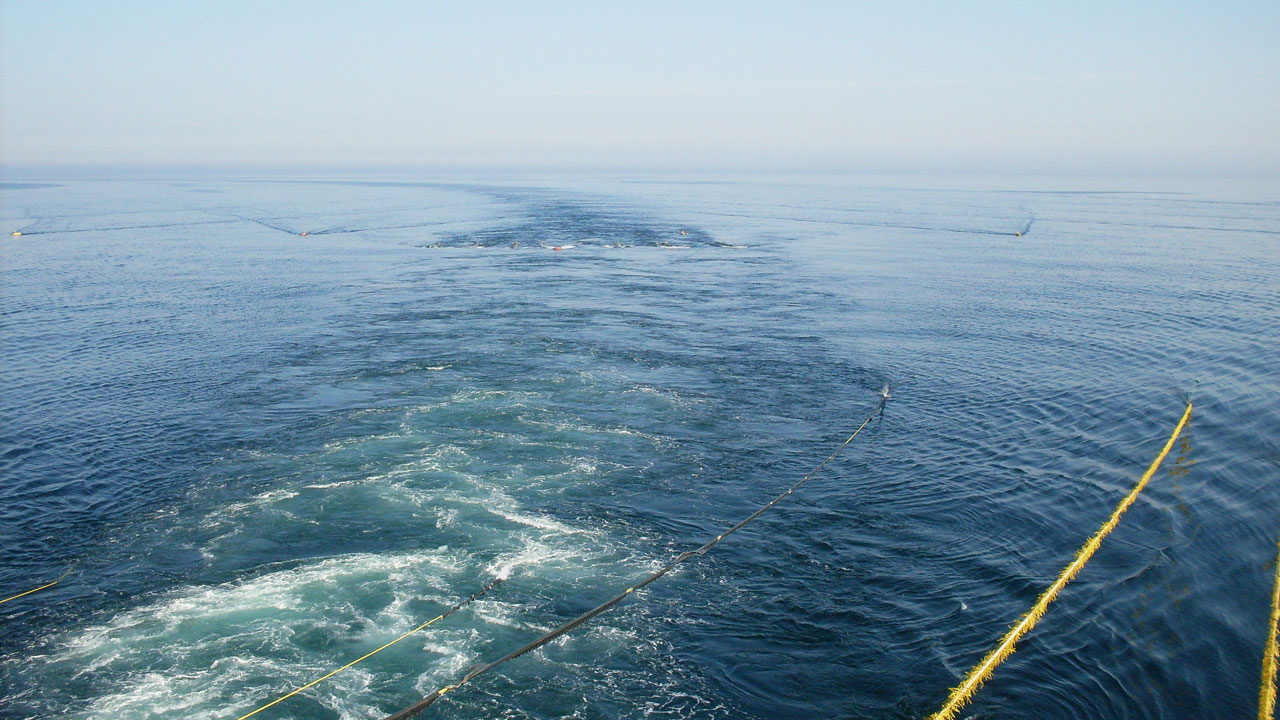 A view across the sea with yellow tow ropes connected to equipment below the surface which is creating a trail in the water as it is towed along