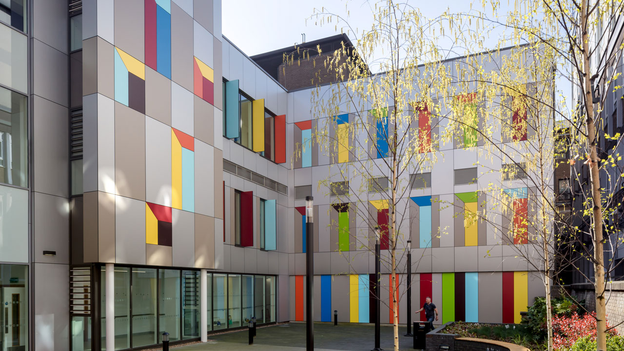 Colorful facade of a modern building with geometric patterns and large windows, surrounded by trees