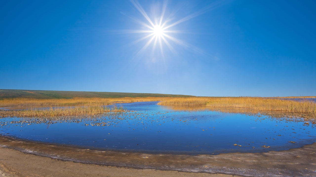Image of a saline reservoir under a blue sky with the sun directly above