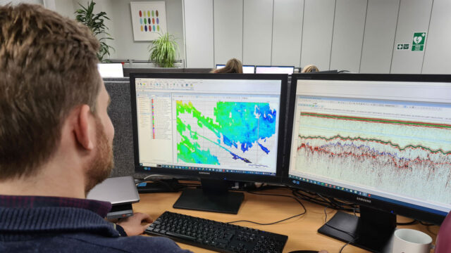 Employee working on a computer with two screens showing geological data and graphs