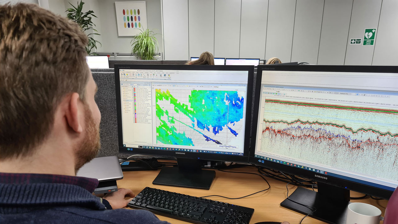 Employee working on a computer with two screens showing geological data and graphs