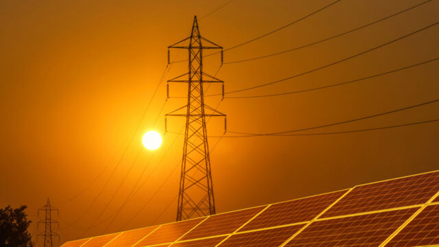 Rows of solar panels with silhouette high voltage electric pylon pillar substation against a sunset