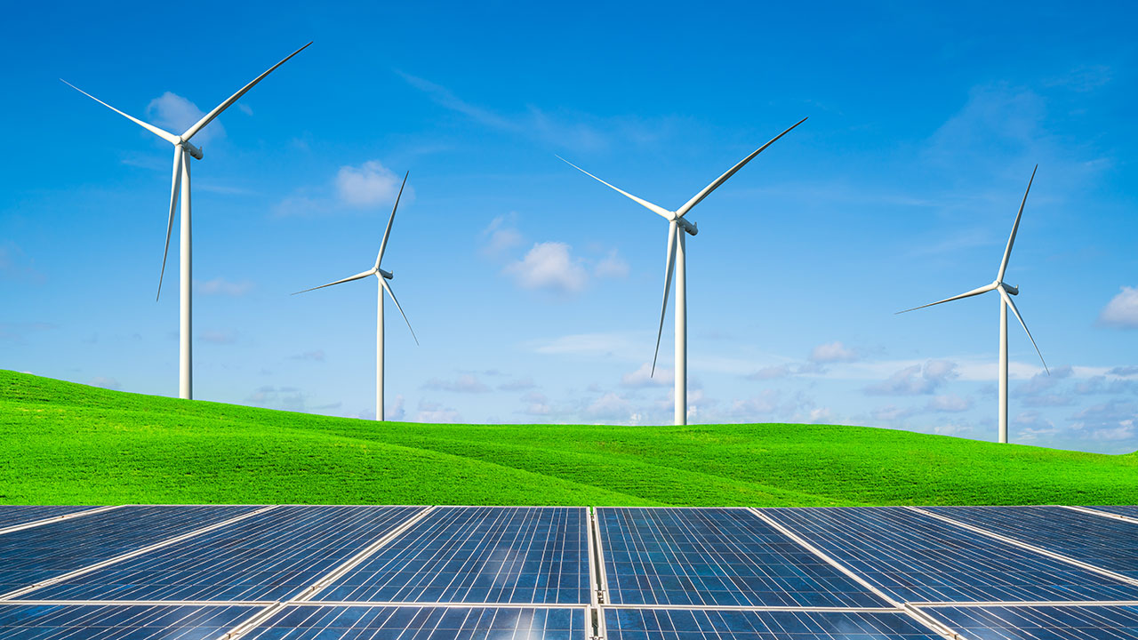 Four wind turbines on a grassy hill behind an array of solar panels