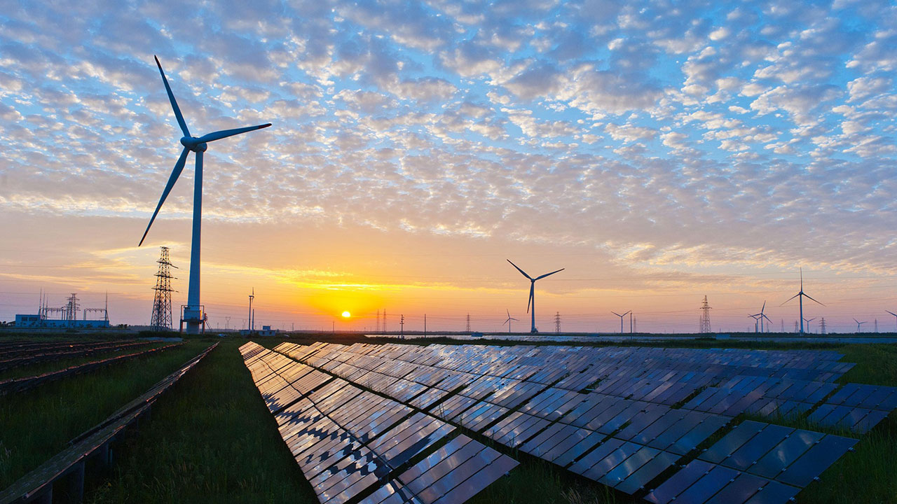 Solar panels and wind turbines at sunset represent Tetra Tech renewable energy engineering