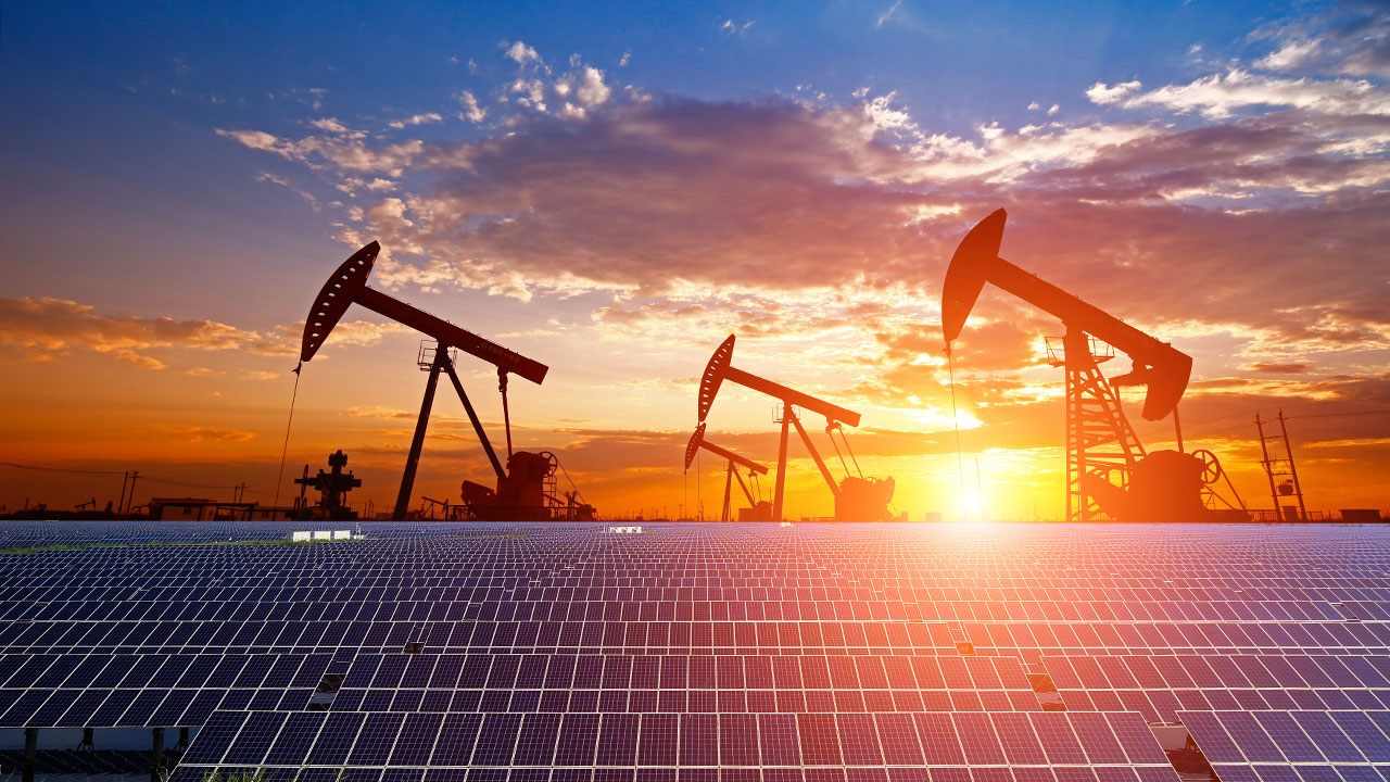 Solar panels in front of oil derricks at sunset represent Tetra Tech’s energy transition services