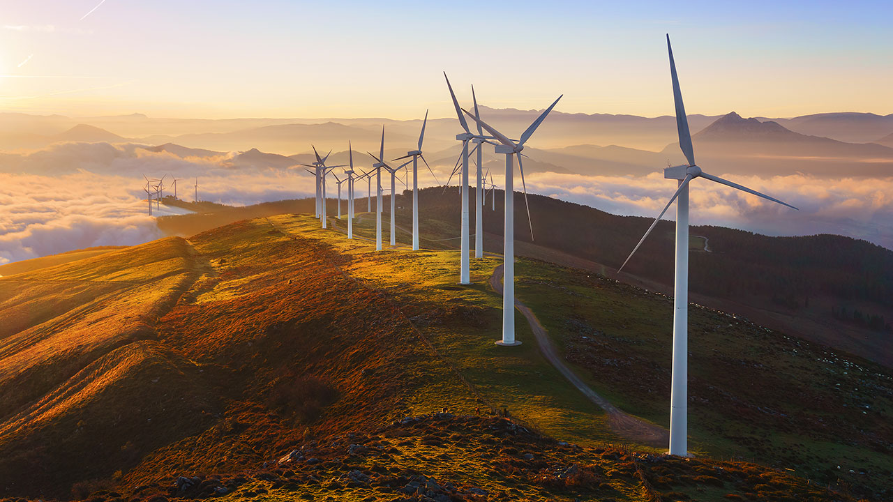 Wind turbines lined up on top of a mountain at sunrise