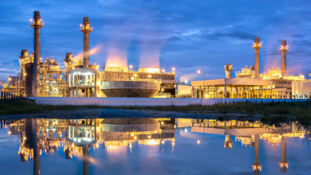 Combined cycle power plant lit up at night against a darkening sky