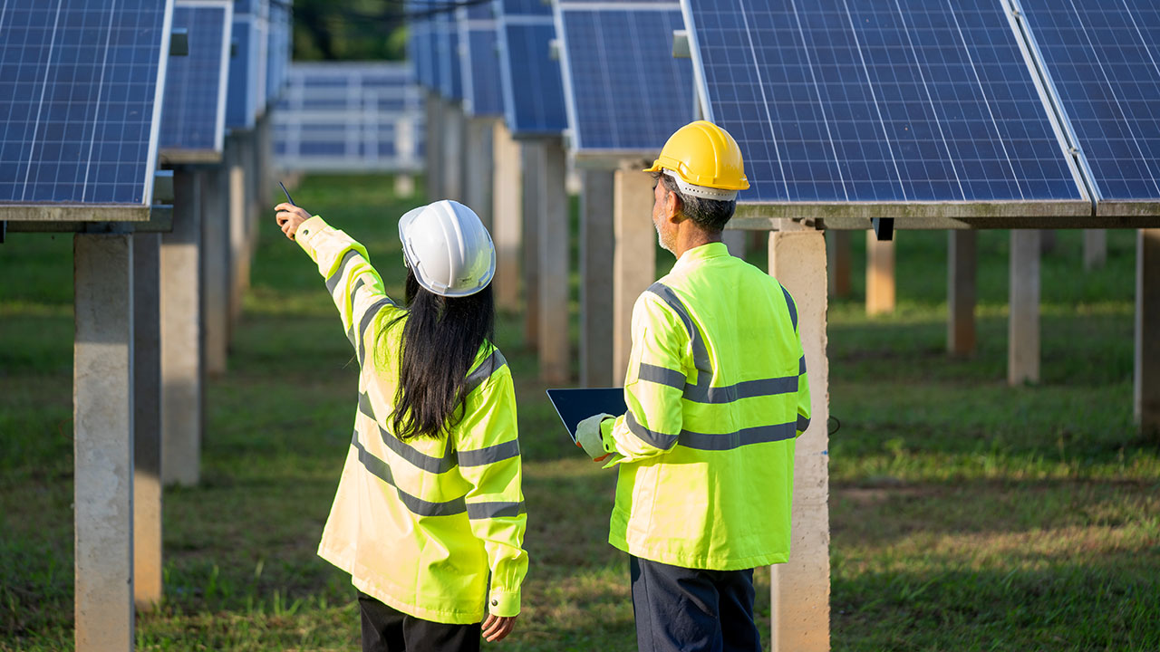 Two engineers in hard hats with laptop discuss solar panels