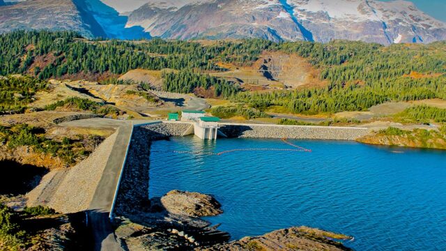 A hydroelectric facility beside a lake and snowy mountains