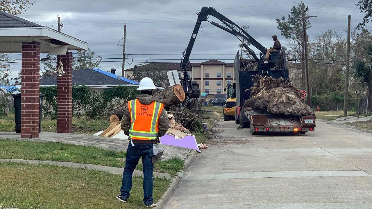 A Tetra Tech employee monitors a crane as it picks up disaster debris along a roadway on a cloudy day