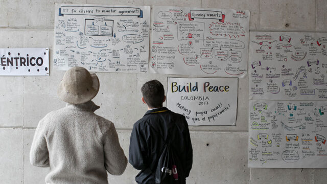 Two men in Colombia look at wall with posters from a citizen participation workshop focused on peacebuilding