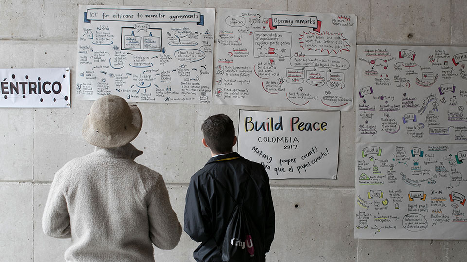 Two men in Colombia look at wall with posters from a citizen participation workshop focused on peacebuilding