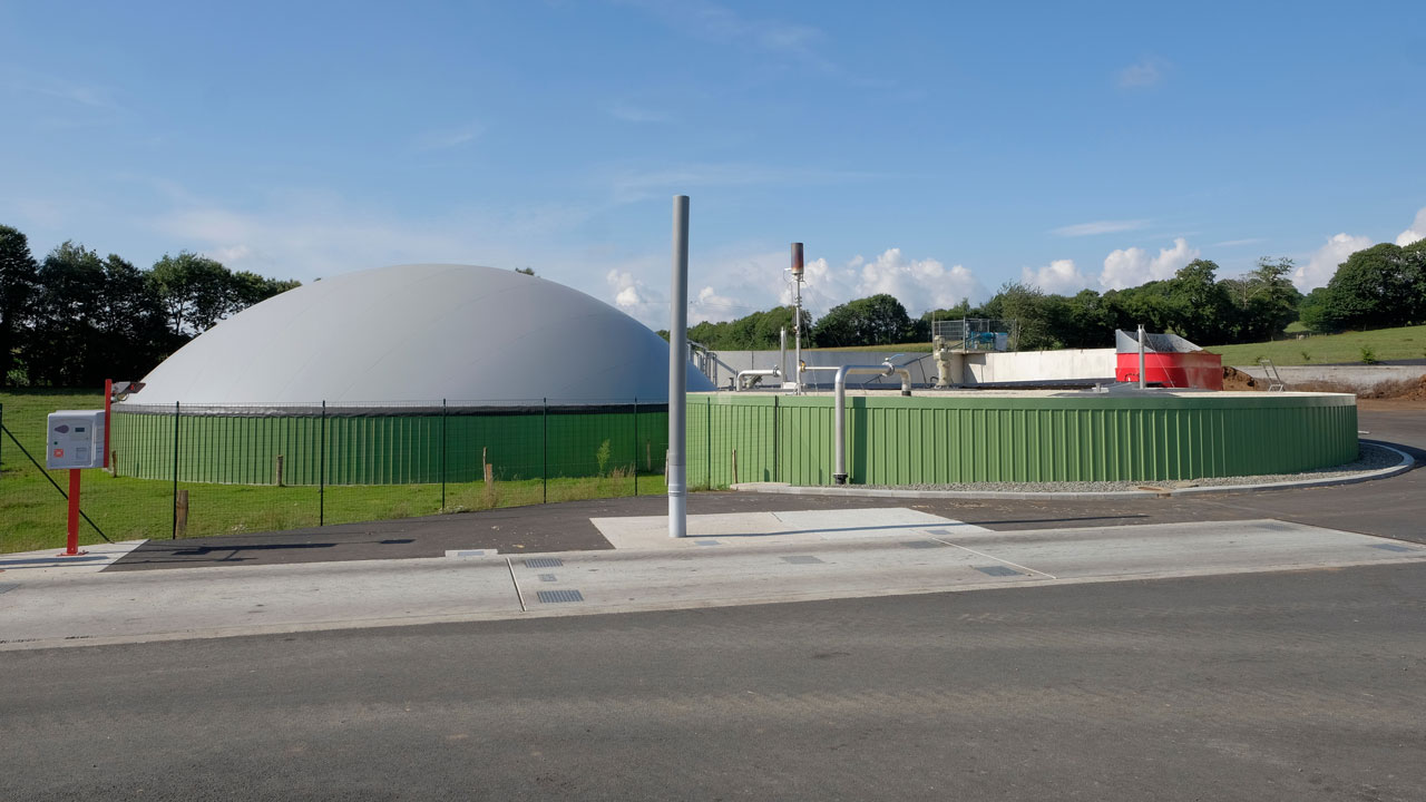 Anaerobic digestion facility for conversion of organic waste with fencing around it and a blue sky in the background