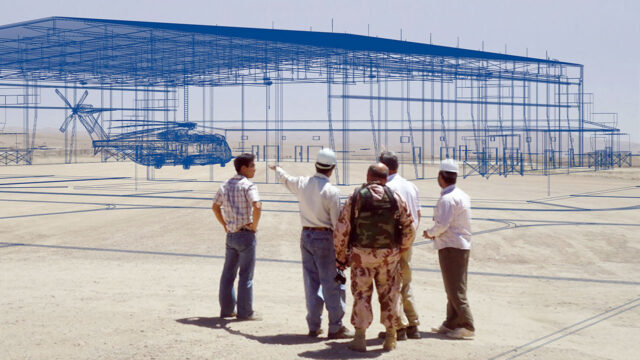 Five men standing outside looking at a 3D rendering of a hangar and helicoprter