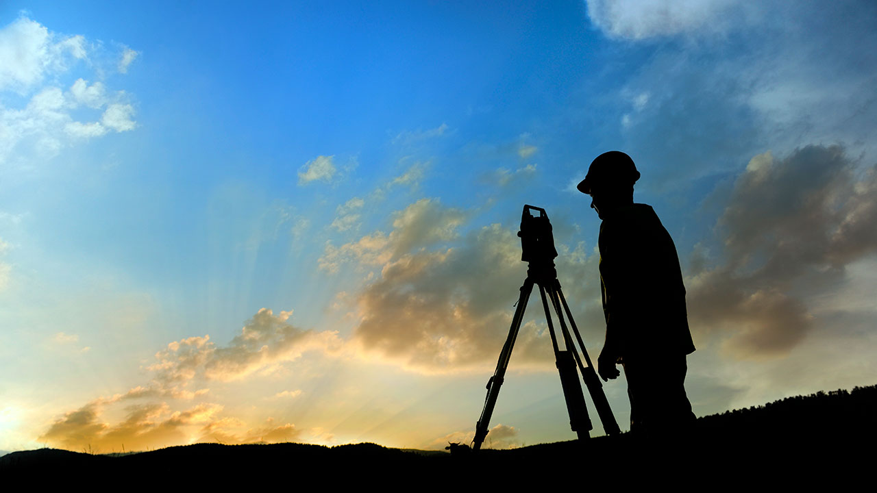Silhouette of a person wearing a hard hat looking through a total station
