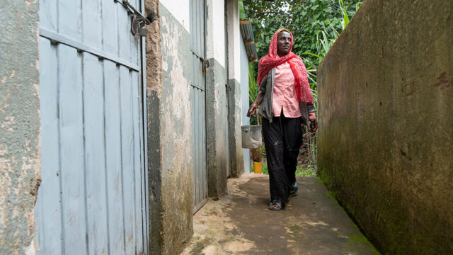 A person walking with a bucket through a latrine block, infrastructure that Tetra Tech aims to make more sustainable