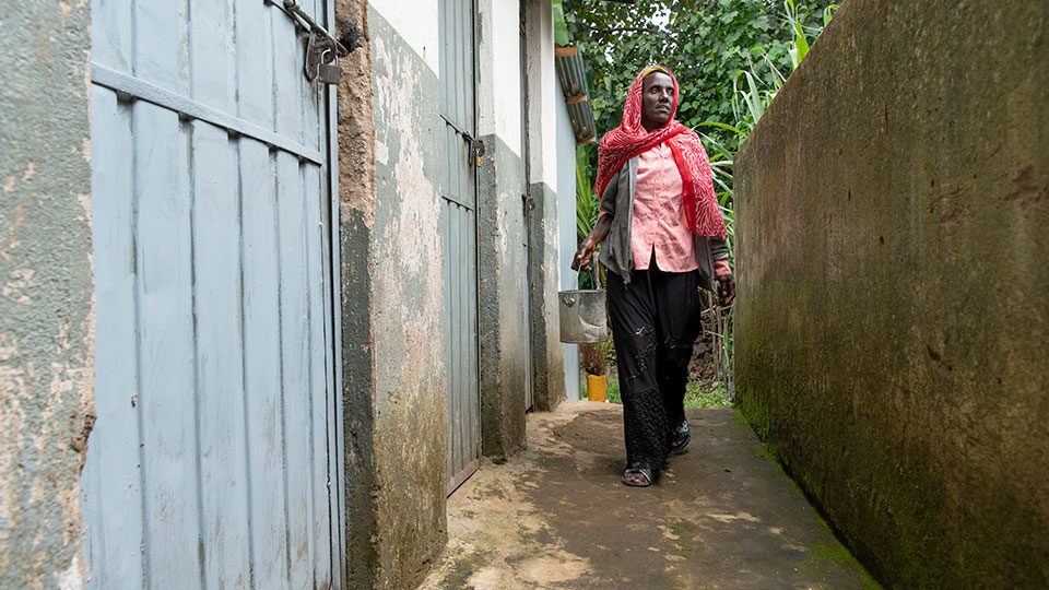 A person walking with a bucket through a latrine block, infrastructure that Tetra Tech aims to make more sustainable
