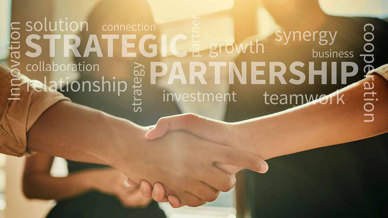 A close up of two people shaking hands with words like strategic, growth, and partnership overlaid in light text on the image