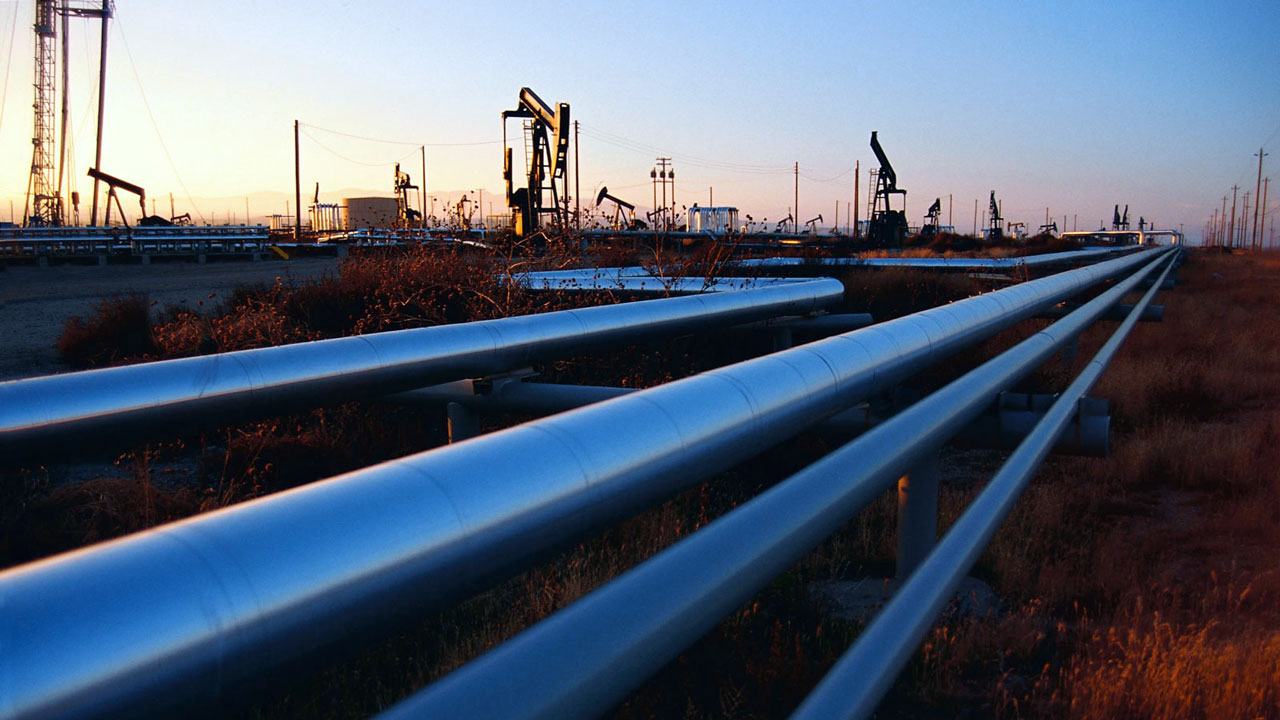 Blue metallic pipelines running through oil field at sunset
