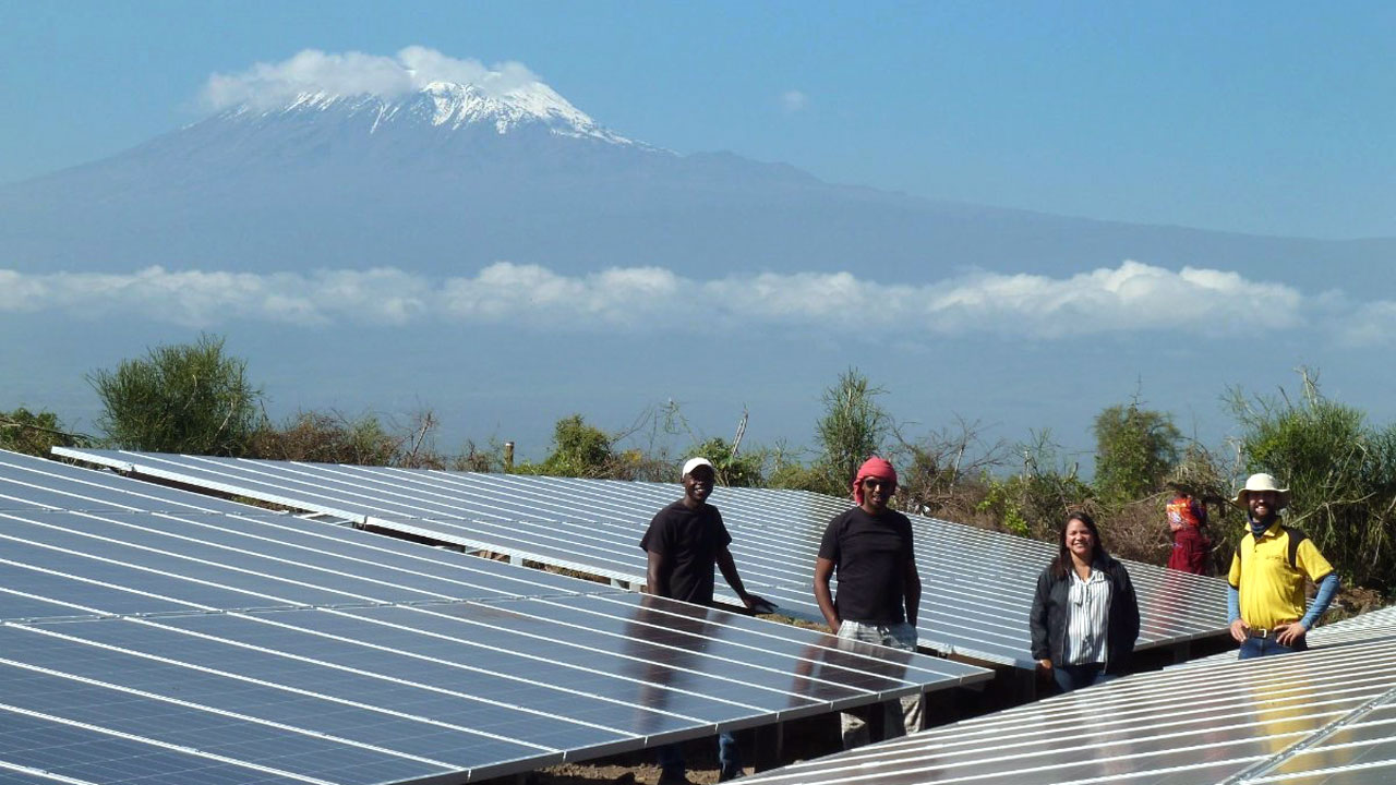 Group of solar engineers stand in a solar panel field at the base of Mt. Kilimanjaro as part of the Tetra Tech-led Power Africa program