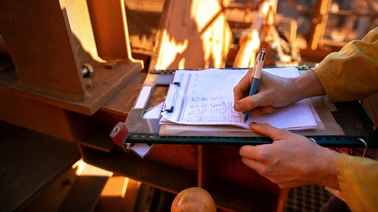 A close up of hands writing notes on a clipboard at a construction site