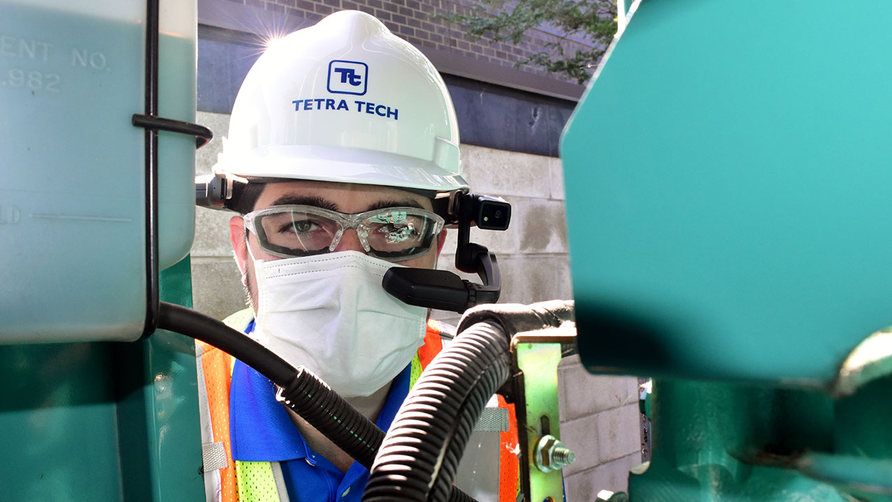 A Tetra Tech employee wearing safety equipment posing with equipment at a project site