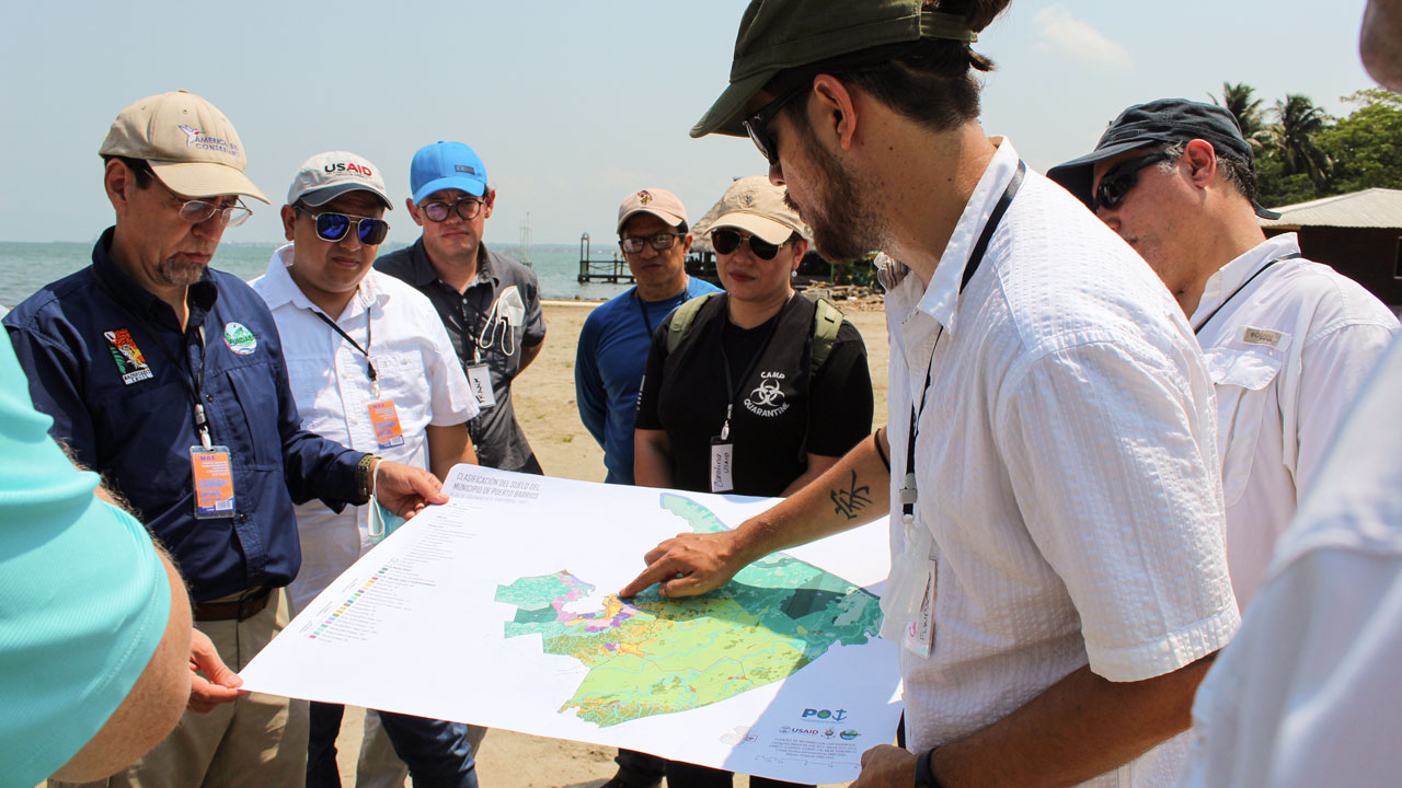 An individual in Colombia holds a map and points to a location with a group of people working in a target region of the Colombia governance program, led by Tetra Tech