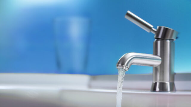 Water flows out of a faucet against a blue background, representing Tetra Tech’s drinking water services