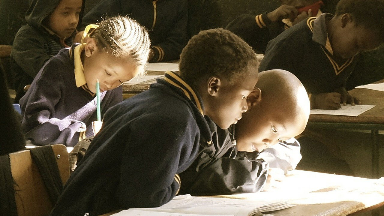 Young children lean over desks in a classroom