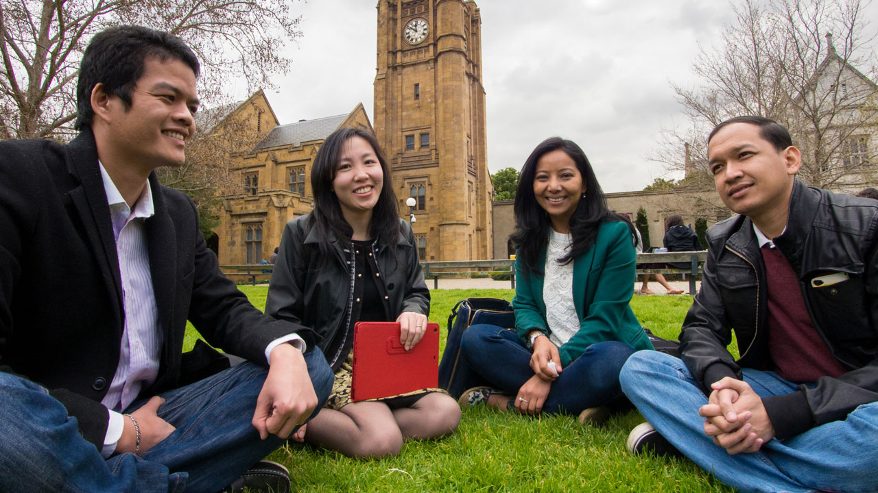 Four students sitting on grass on a campus