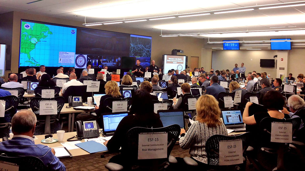 A control room full of communication employees with laptops and phones