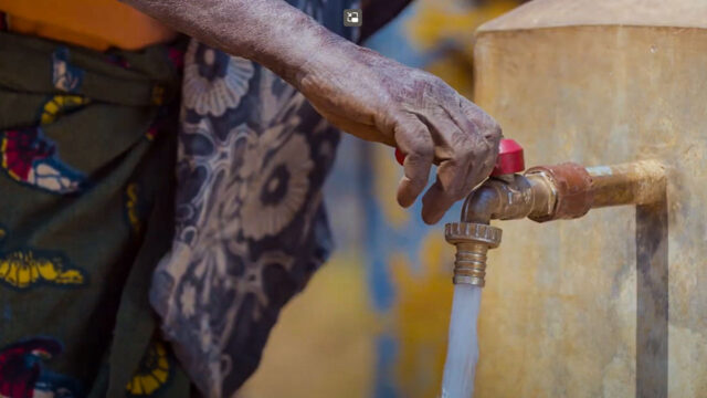 A closeup shot of a hand turning on a tap with water flowing out