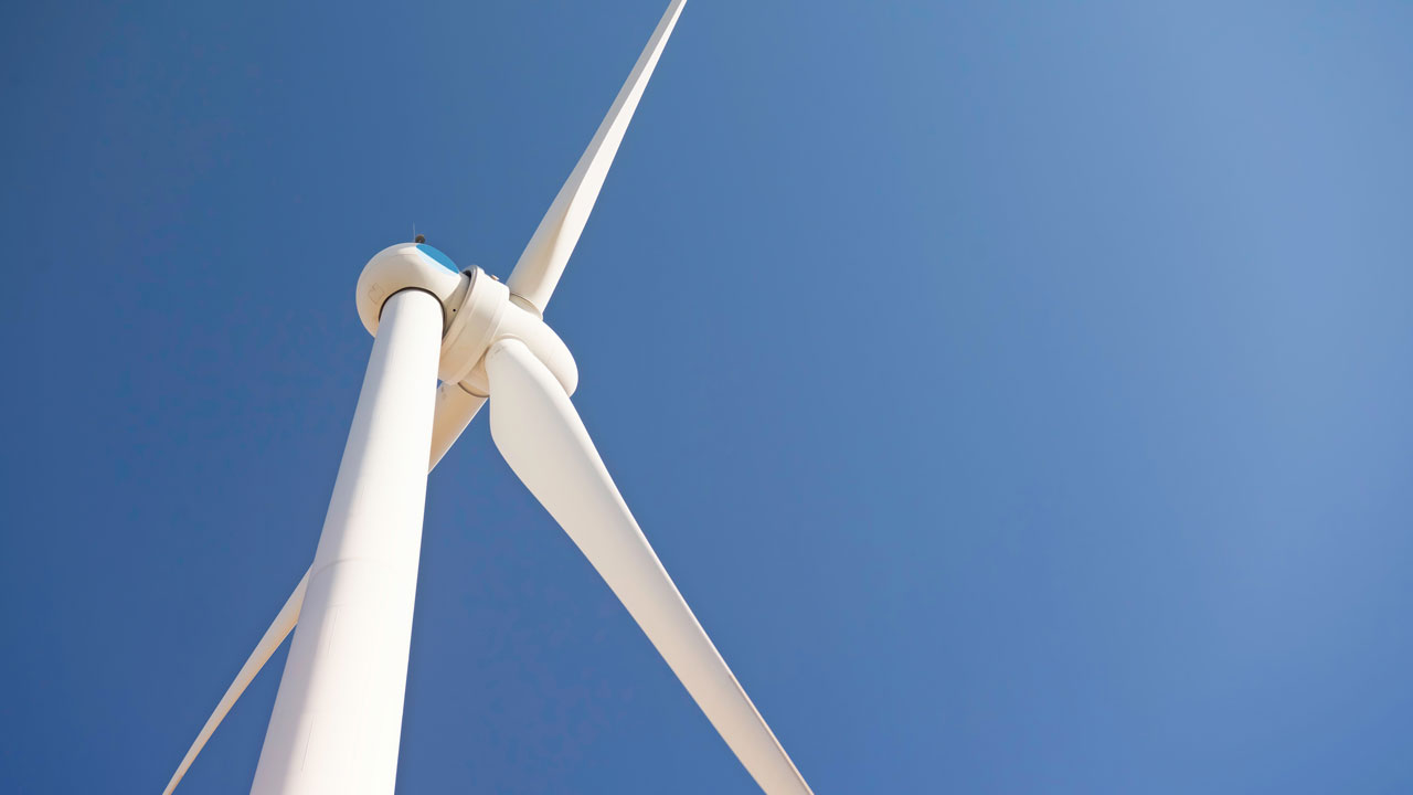 A wind turbine stands against a bright blue sky