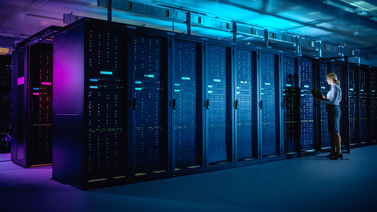 IT Technician running maintenance program on Laptop at a modern telecommunications operational data center in neon light