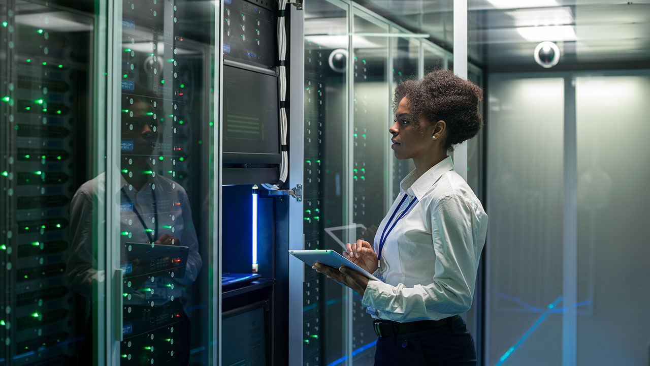 Female technician working on a tablet in a data center full of rack servers running diagnostics and maintenance