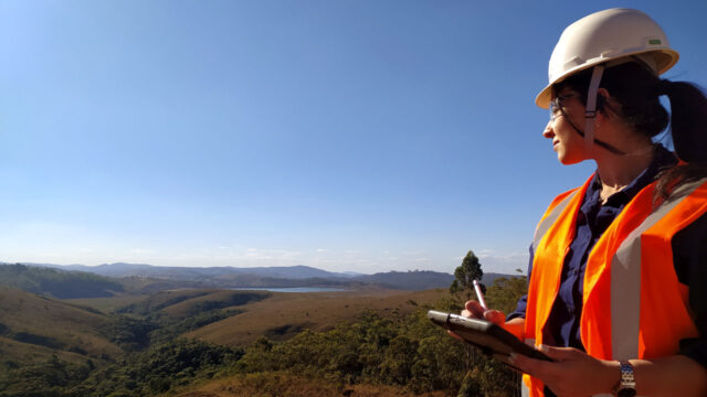 Worker wearing safety gear and holding a tablet looking towards a green landscape