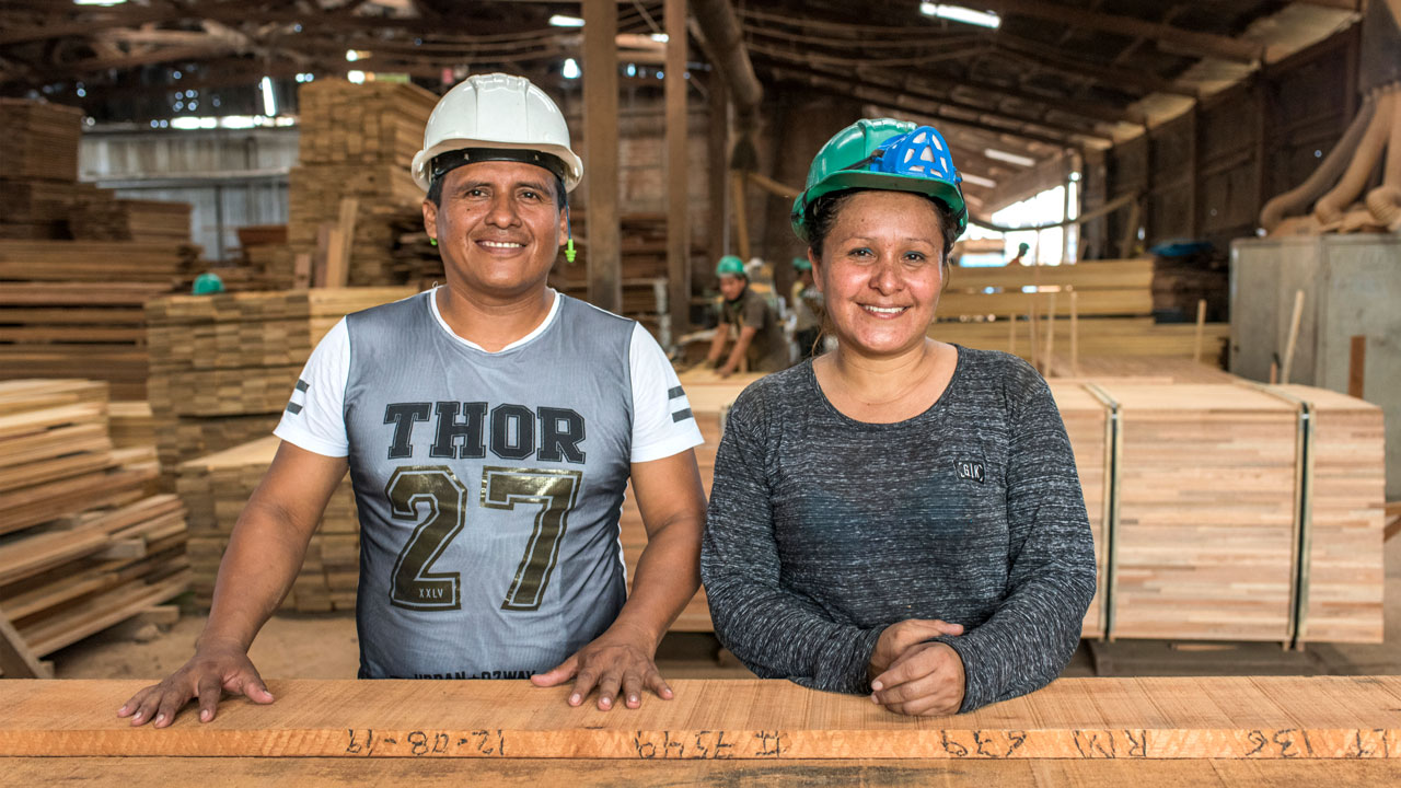 A woman and man stand in front of sustainably produced lumber as part of the Tetra Tech-led forestry program in Peru