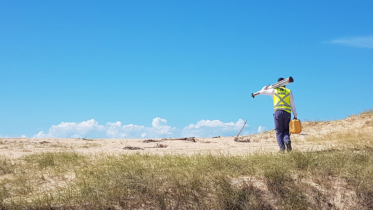 A Tetra Tech employee walking in the sand holding equipment in both hands