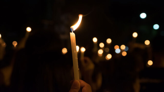 Hands holding lit candles at a night vigil