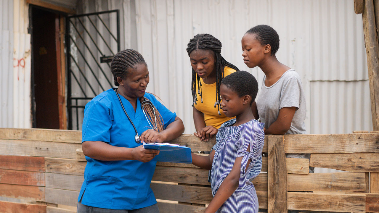 Three girls stand looking at a tablet held by a female doctor in South Africa