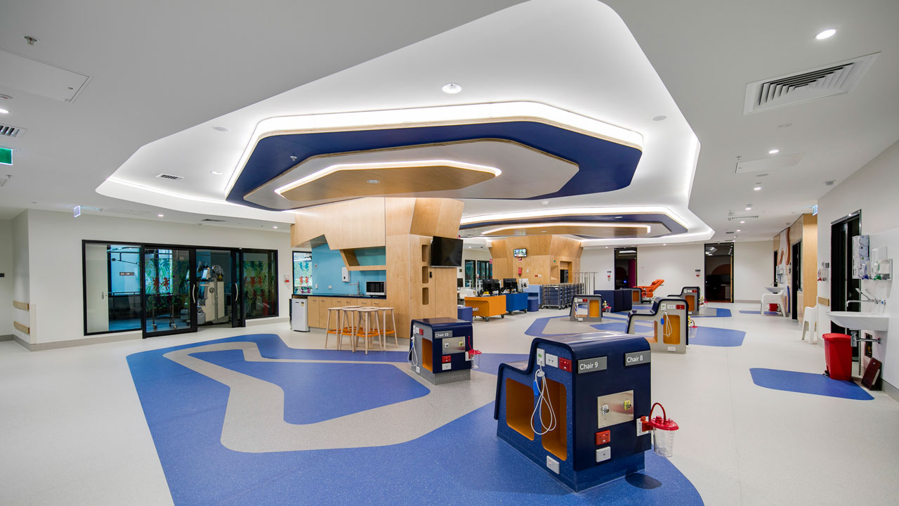 A hospital treatment area with blue and white geometric designs on the floor that are echoed in the ceiling and lighting treatment