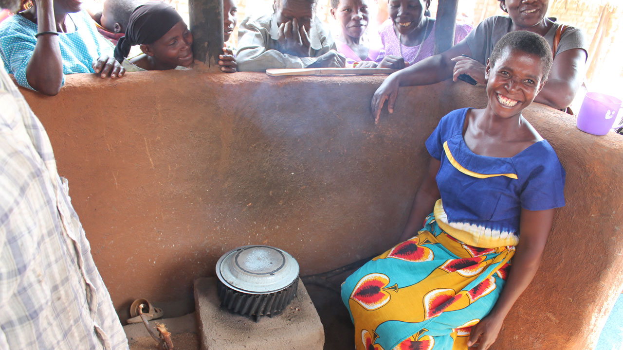 A woman sits beside her modern cookstove, an initiative supported by the Tetra Tech-led clean cooking project in Malawi
