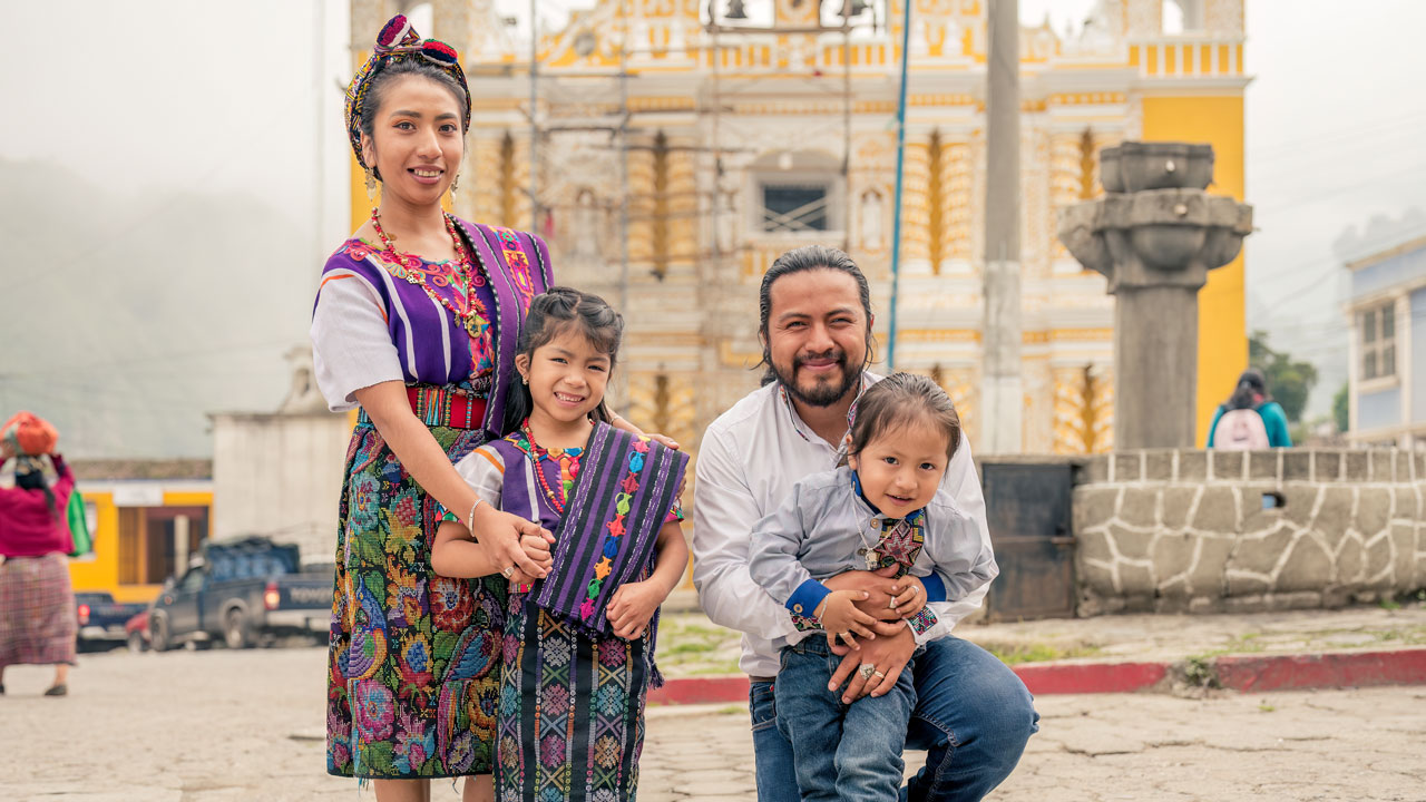 A family in traditional dress poses outdoors in a town square in Guatemala