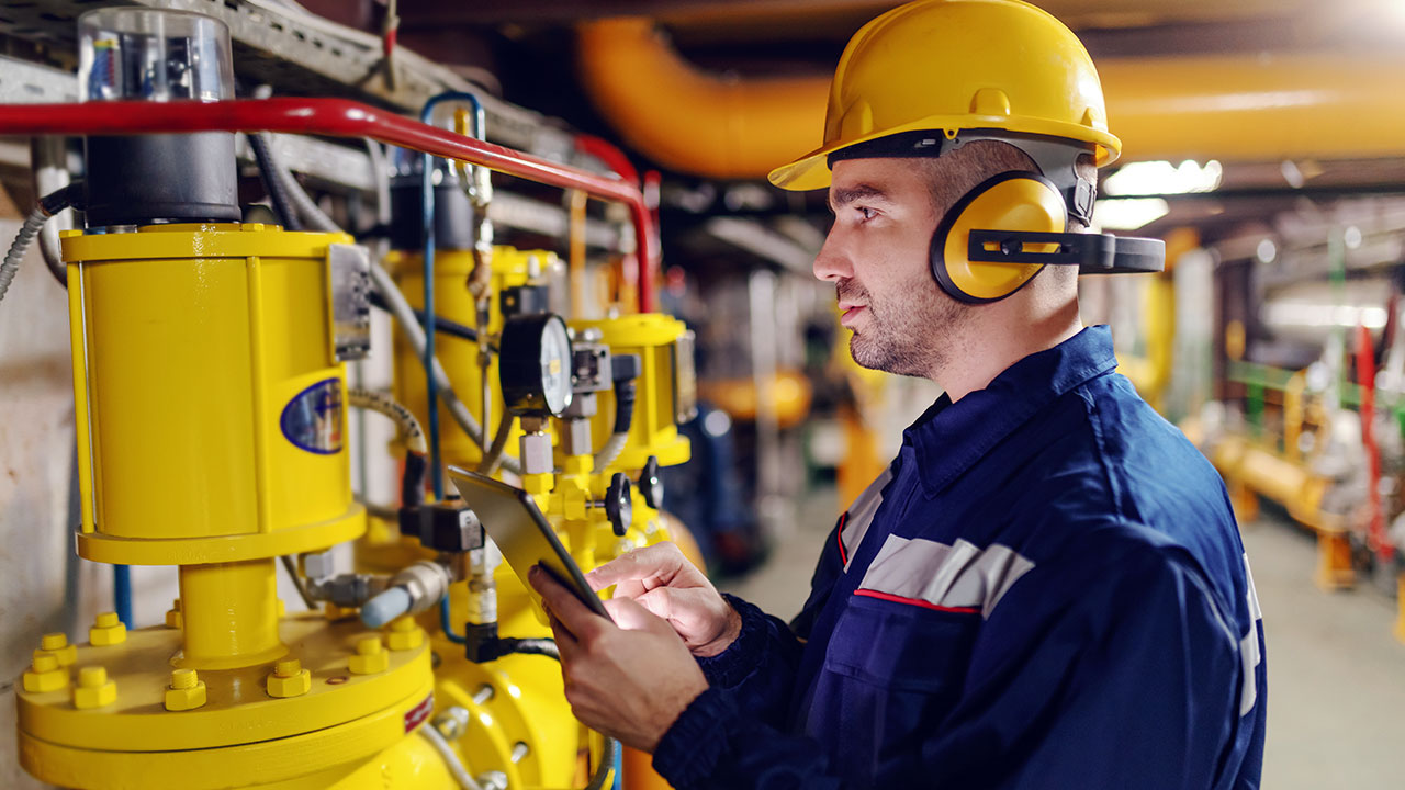 A person wearing a helmet, antifones and in protective suit checking air pressure on boilers