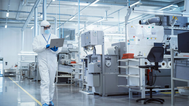 Scientist in sterile coverall walking with laptop computer in a lab