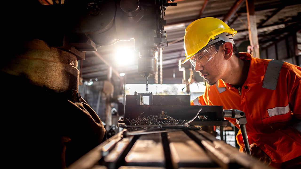 A person wearing orange work clothes and glasses stands beside the drilling rig and use metal drills in industrial
