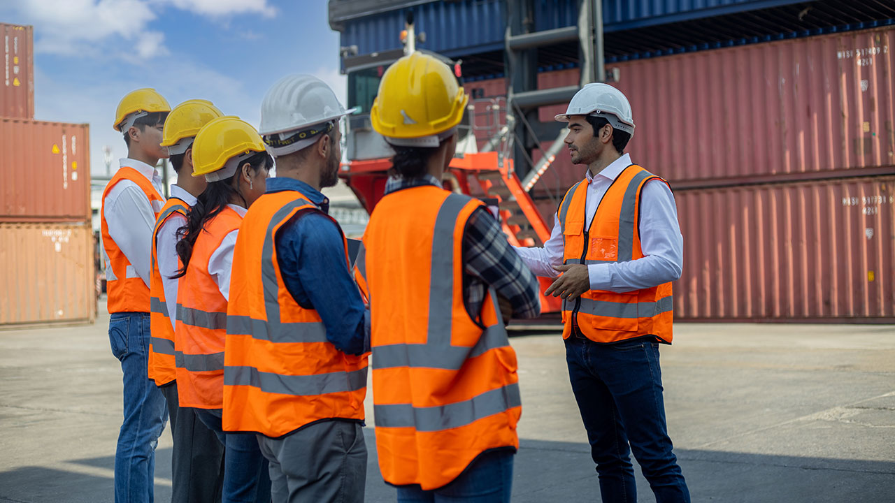 Four people wearing orange vests and hard hats gather for a meeting at a project site